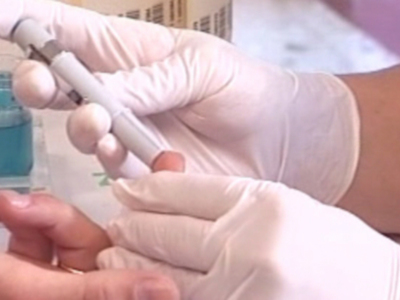 Un dedo se prepara para una prueba de sangre con un dispositivo médico, mientras que la mano del paciente sostiene su dedo.