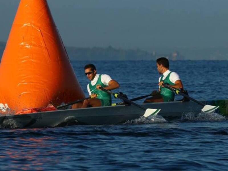 Barco de vela con dos personas a bordo, navegando en el agua azul.