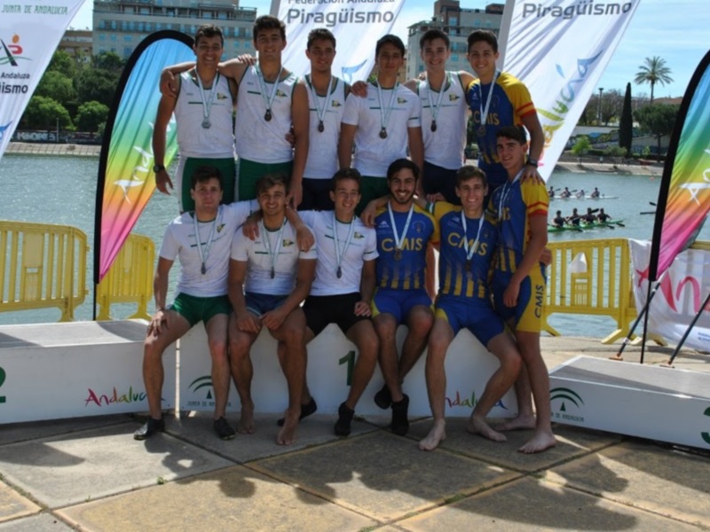 Equipo de piragüismo celebrando en el podio con banderas y logotipos.