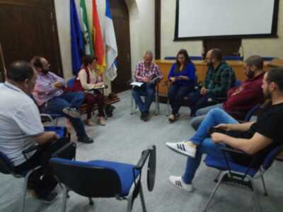 Reunión de trabajo en una sala de conferencias con personas sentadas en sillas y banderas en el fondo.