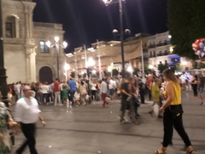 Noche en la plaza de España, Sevilla, con luces y gente caminando.
