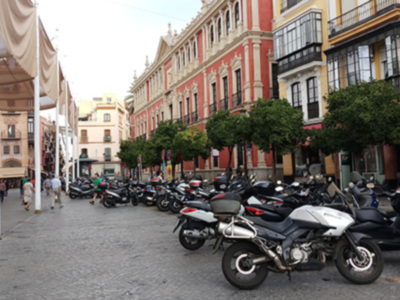 Calle con motocicletas aparcadas, edificios antiguos y gente caminando.