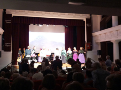 Concierto en un teatro con público sentado y músicos en el escenario.