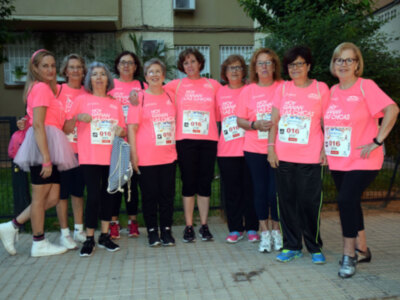 Grupo de mujeres con camisetas rosadas y medallas, posando en una calle.