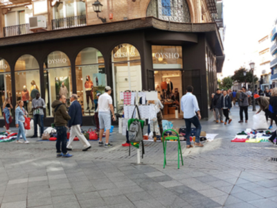 Mercado de ropa usada frente a una tienda Oysho en una calle urbana con gente caminando y comprando.