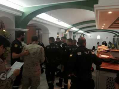Una imagen de varios oficiales militares y civiles reunidos en un comedor militar, con mesas y sillas. El ambiente es formal y ordenado, destacando la presencia de uniformes militares y civiles.
