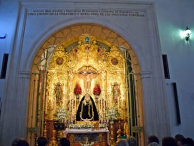 Interior de una iglesia con un altar dorado y oro, adornado con flores y estatuas religiosas. La pared tiene inscripciones en latín sobre la Virgen María y Cristo.