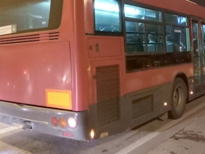 Un autobús rojo está estacionado en una calle nocturna, con luces de freno encendidas y ventanales oscuros.