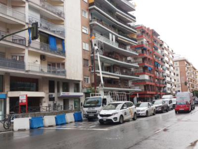 Vehículo de mantenimiento en una calle residencial con edificios de apartamentos y coches estacionados.