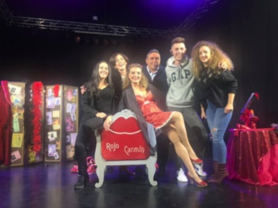 Equipo de teatro posando en escenario con silla roja y decoración festiva.