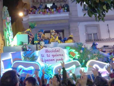 Carroza de Carnaval con letrero "Recicla, sí tú quieres". Personajes animados y decoraciones coloridas. Público participando activamente.