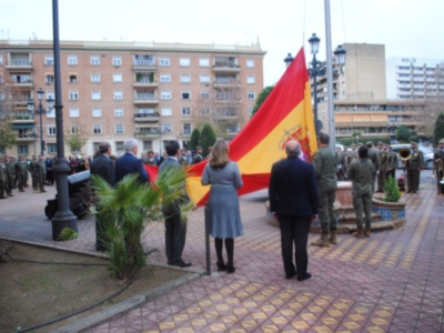 Una imagen de una ceremonia militar en un entorno urbano con soldados y oficiales, ondeando la bandera española.