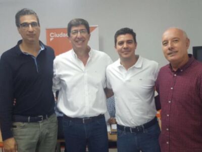 Un grupo de personas posa frente a una pared con un cartel que dice "Ciudadanos". El ambiente parece ser informal y relajado, posiblemente en una reunión o evento.