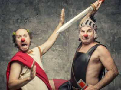 Un personaje con una nariz roja y una armadura de gladiador sostiene una espada, mientras otro personaje con un tocado de gladiador levanta la mano. Ambos personajes parecen estar en una escena de combate.