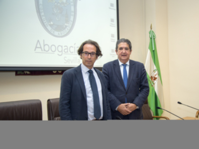 Dos hombres en trajes posan frente a una pantalla con el logo de Abogacía Sevilla.