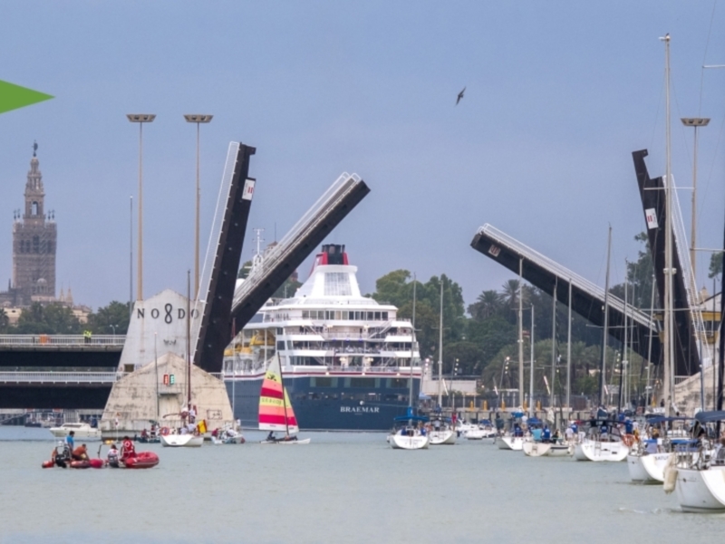 Puerto de Sevilla, con el Cristo de la Sangre y el Puerto Real al fondo. Barcos en el puerto, banderas y logotipos de Círculo Náutico Sevilla y XV Centenario Puerto Real.