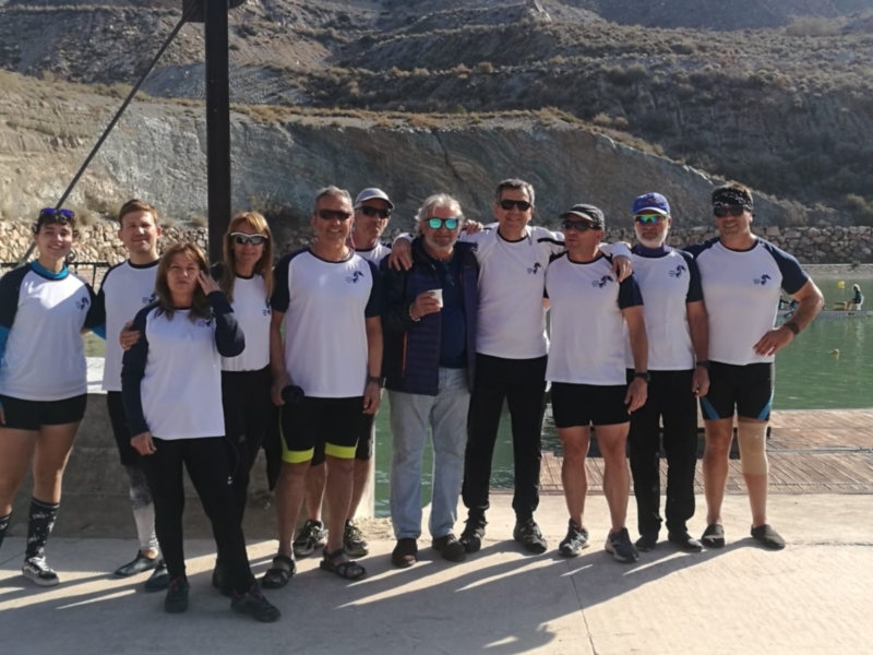 Equipo de remo posando frente al río, vestidos con camisetas blancas y negras. Fondo de montañas y agua cristalina.