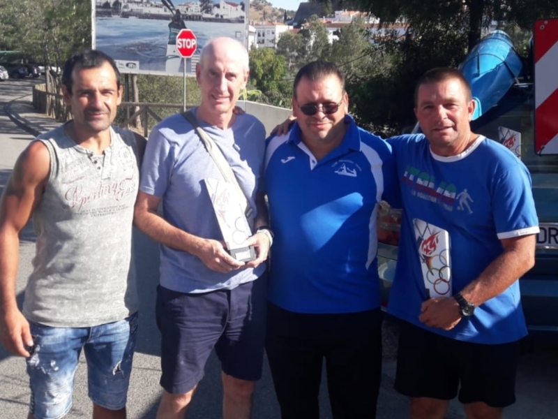 Grupo de personas posando con un trofeo, frente a una carretera con carteles y árboles.