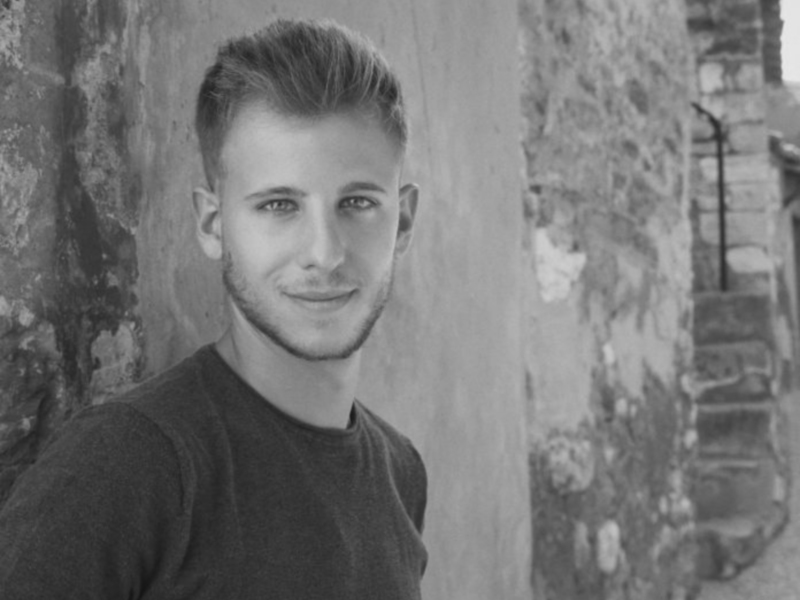 Retrato en blanco y negro de un joven sonriente frente a una pared texturizada.