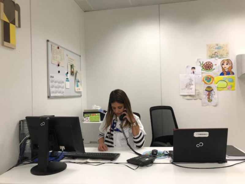 Persona trabajando en un escritorio con un teléfono y un ordenador, en un espacio bien iluminado con decoración infantil en la pared.