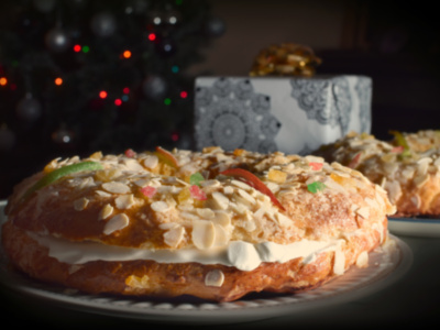 Pastel de Navidad con crema y frutas secas, sobre un plato blanco. Fondo borroso con luces navideñas y una caja de regalo.