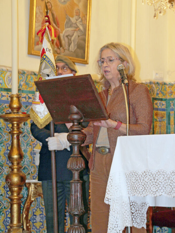 Mujer hablando en un evento formal en un ambiente con decoración religiosa y ornamentos tradicionales.