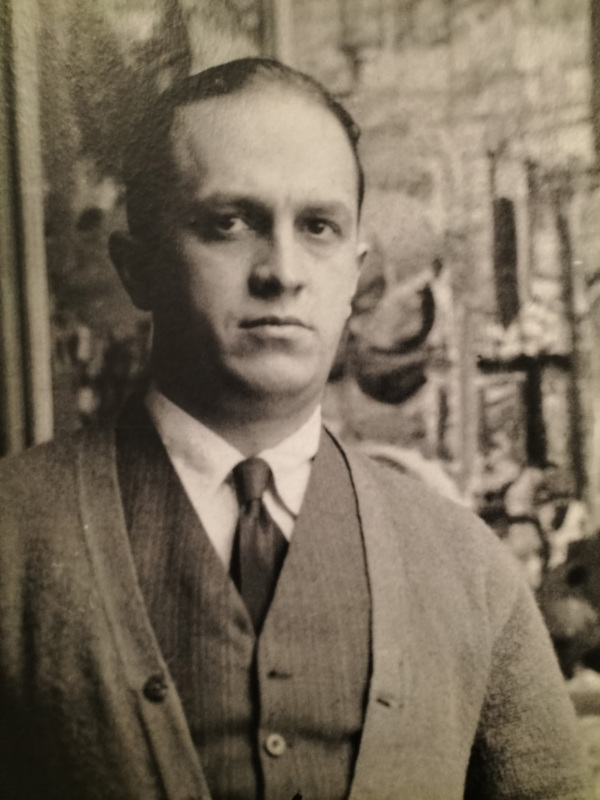Un hombre con una camisa blanca, corbata y chaleco de cuadros. La imagen es en blanco y negro.